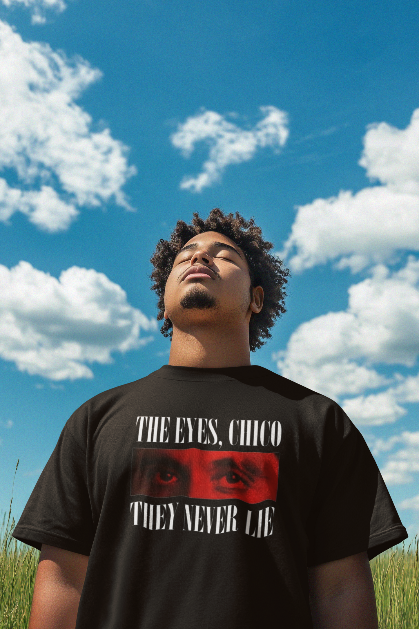 Man wearing oversized Weeknd t-shirt featuring bold eye graphic and quote 'The Eyes, Chico. They Never Lie' under a blue sky