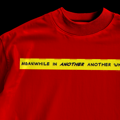 Close-up of yellow comic banner reading Meanwhile In Another Another Universe on amhype red graphic tee front