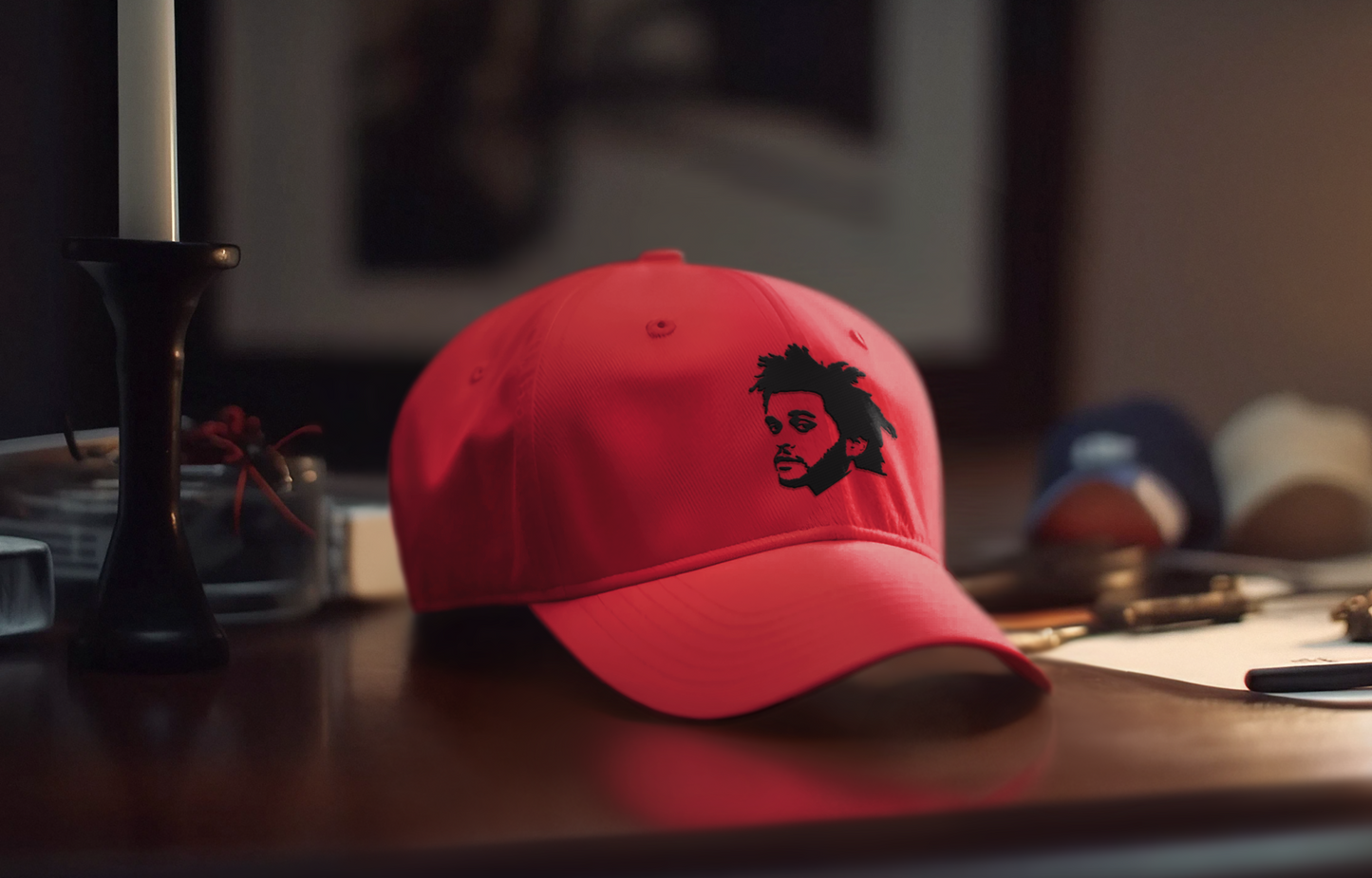 Red embroidered snapback hat featuring The Weeknd’s silhouette, placed on a wooden nightstand in a cozy room setting – XO concert merch by AmHype USA.