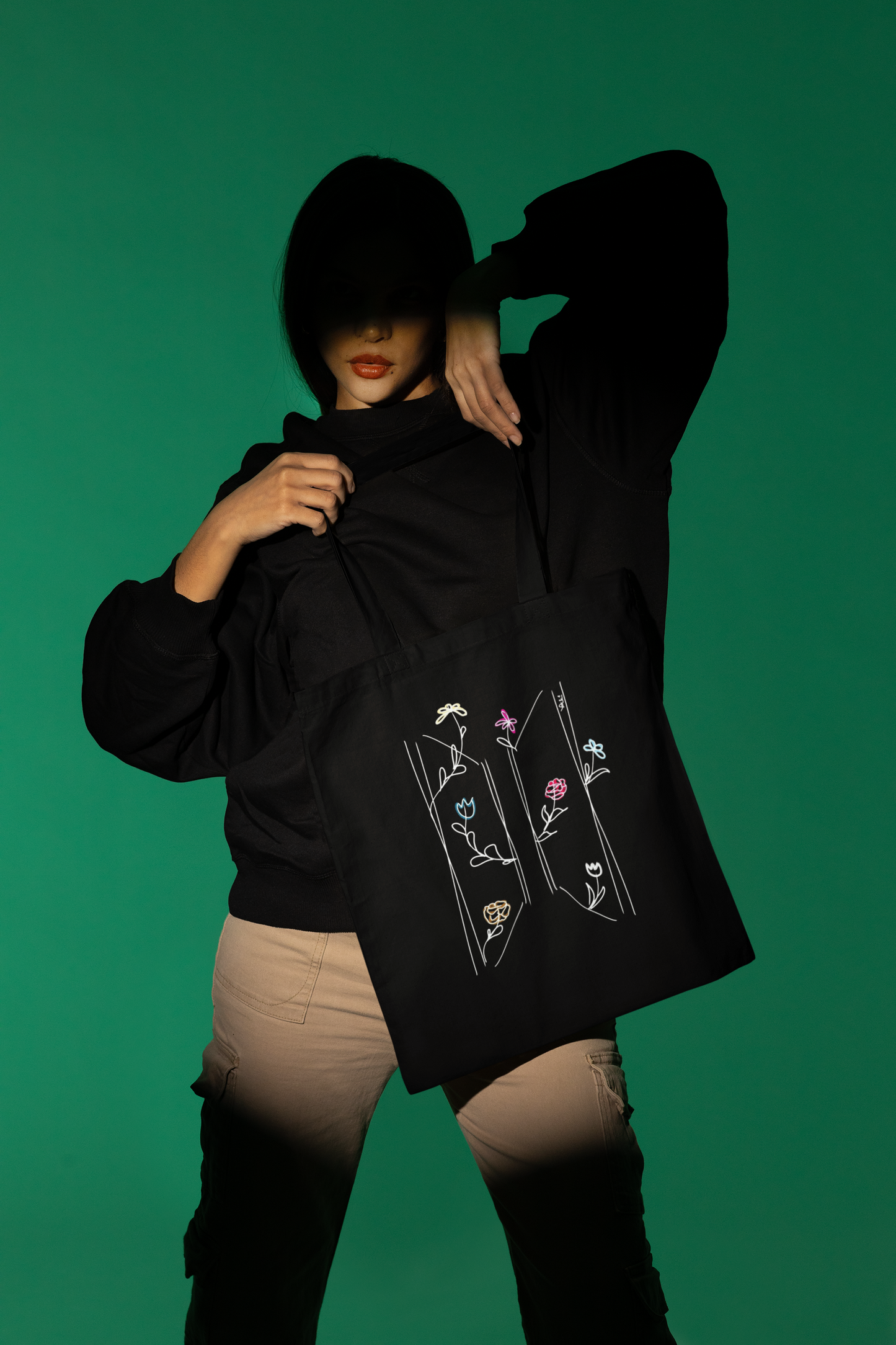 Woman posing with BTS wildflower logo black tote bag in studio — colourful flower line art ARMY merch by amhype