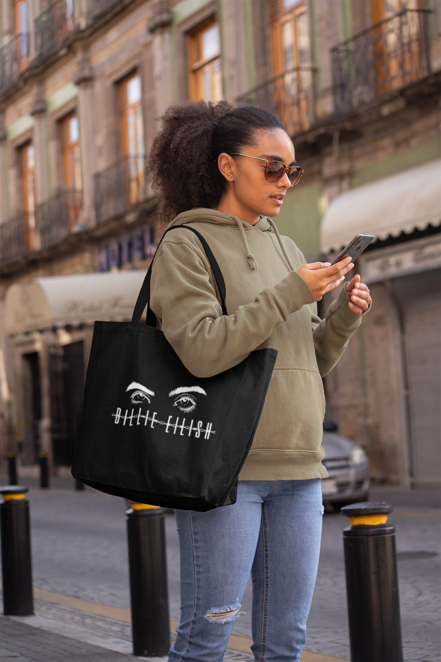 Woman in street carrying Billie Eilish black tote bag — white eye illustration and barbed wire name print by amhype